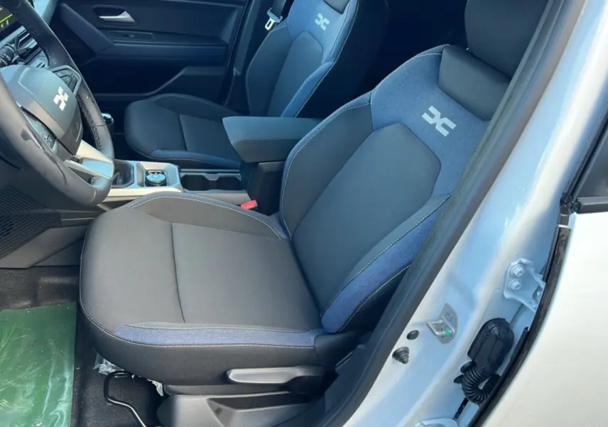 Vue intérieure côté conducteur du Dacia Duster 2025 blanc glacier, sièges tissu noir et bleu avec logo distinctif brodé.