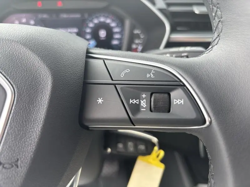 Gros plan sur les commandes du volant cuir noir de l'Audi Q3 blanc Glacier, avec boutons de volume et appel téléphonique.