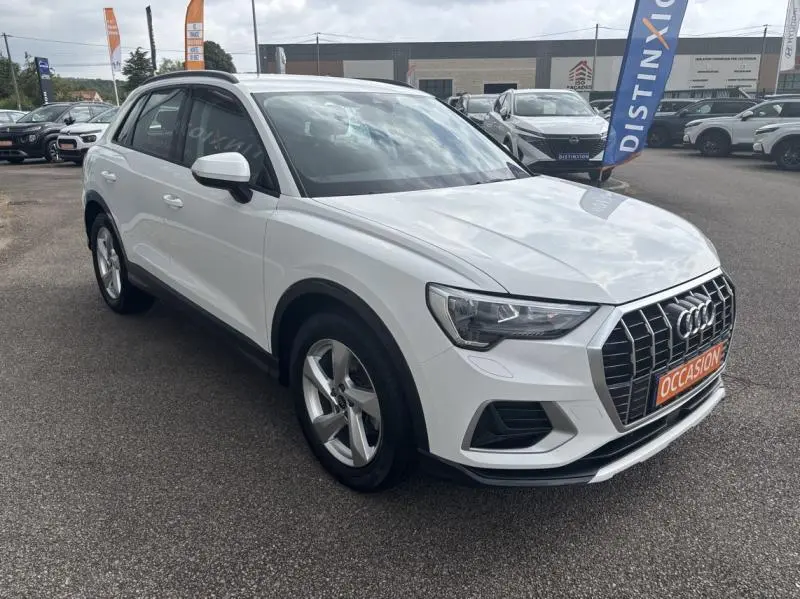 Audi Q3 blanc Glacier métallisé en vue 3/4 avant droit sur parking avec calandre chromée et jantes alu cinq branches.