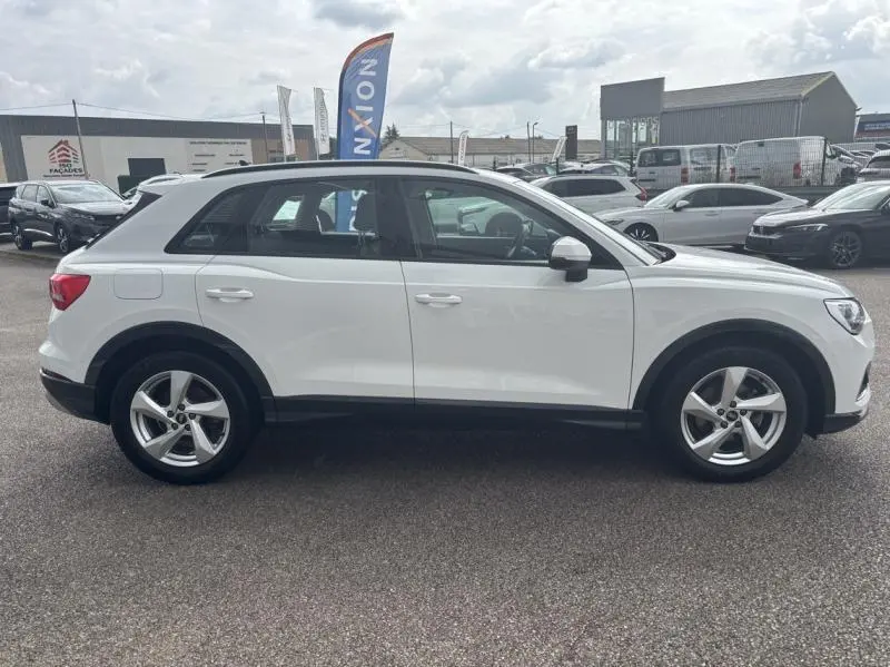 Profil droit d'un Audi Q3 blanc Glacier métallisé 2022, avec jantes alu et vitres légèrement teintées, stationné en extérieur.