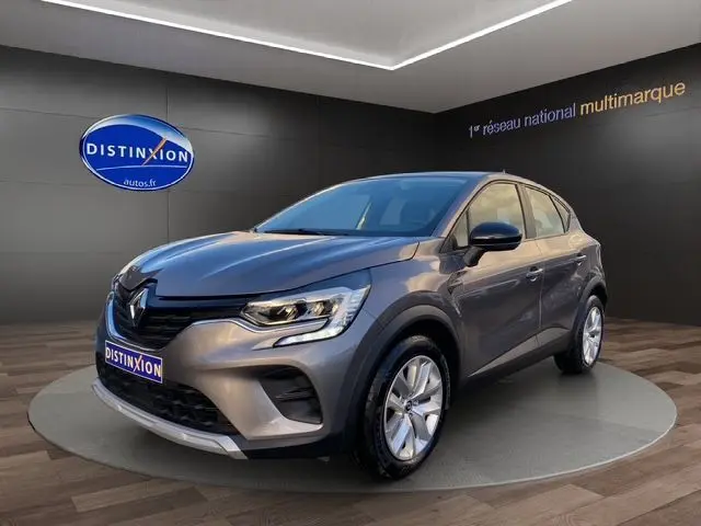 Renault Captur TCE 90 Équilibre gris Cassiopée en 3/4 avant droit, avec jantes argentées et calandre noire distinctive.