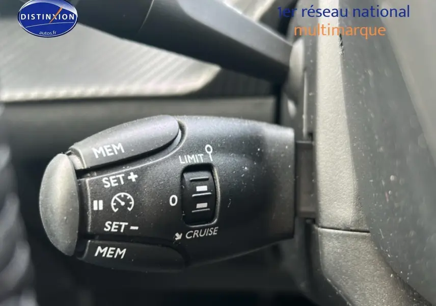 Gros plan sur la commande de régulateur de vitesse noire dans l'habitacle d'une Peugeot 208 gris artense.