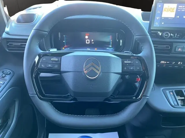Vue rapprochée du volant cuir noir du Citroën Berlingo gris Artense, avec tableau de bord numérique et écran tactile visible.