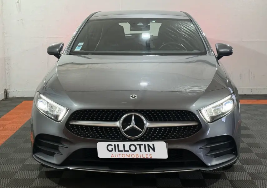 Vue frontale d'une Mercedes Classe A 200 AMG Line gris foncé avec calandre noire à motifs étoilés et phares LED allumés.