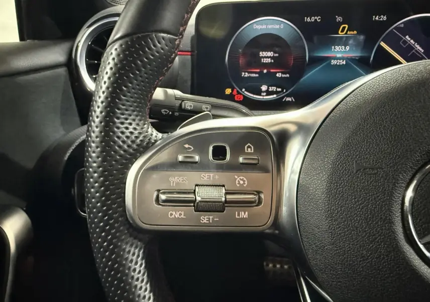 Gros plan sur le volant cuir perforé gris foncé de la Mercedes Classe A 200 AMG Line avec commandes du régulateur de vitesse et tableau de bord numérique.