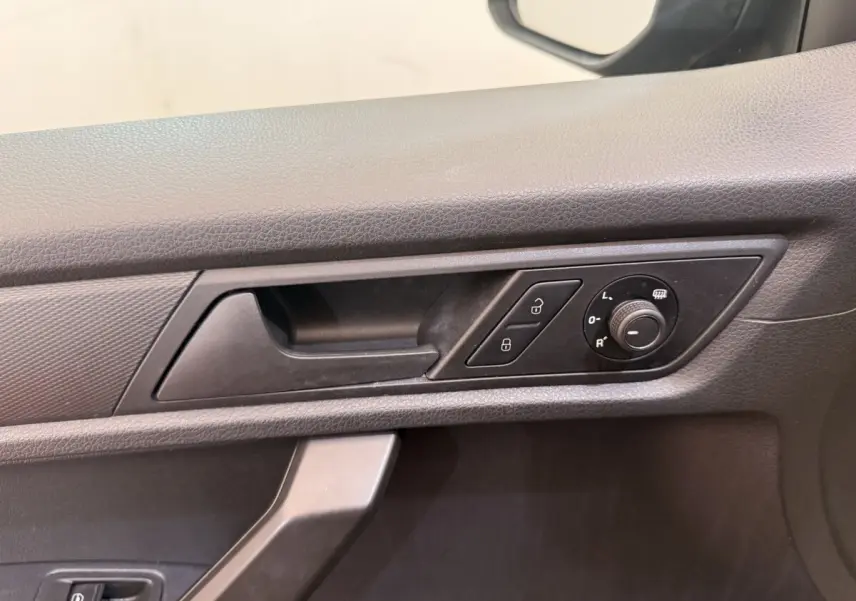 Détail de la poignée intérieure côté conducteur du Volkswagen Caddy noir avec commandes de verrouillage et réglage des rétroviseurs.