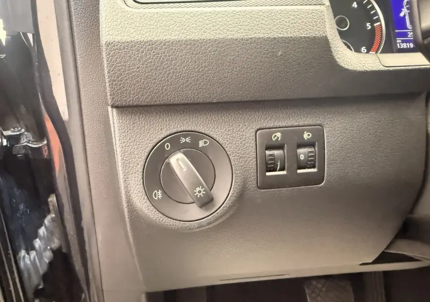 Détail du tableau de bord côté gauche du Volkswagen Caddy noir 2019, avec commandes des phares et réglages lumineux.