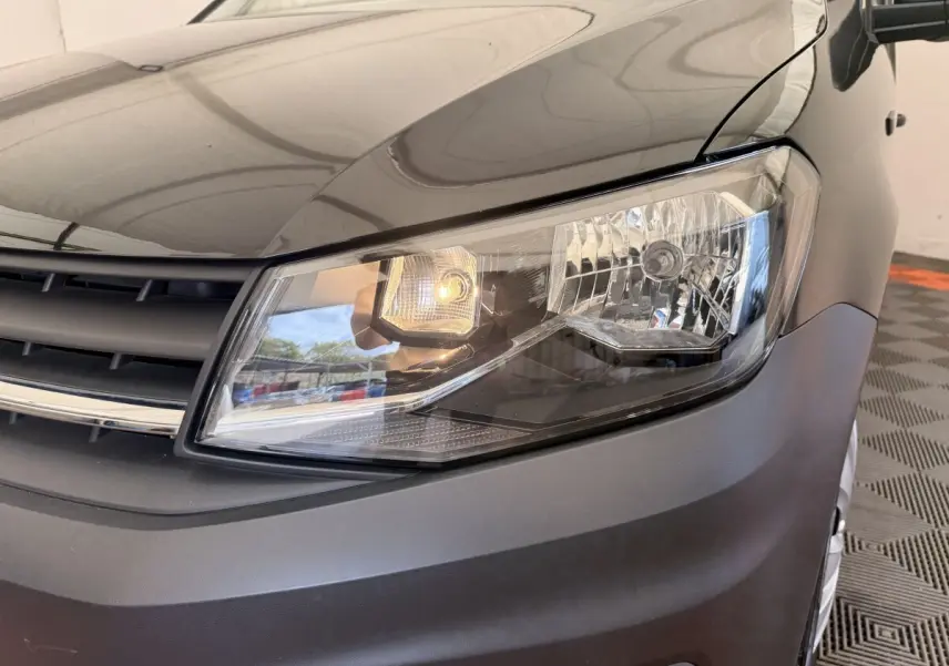 Gros plan sur le phare avant droit du Volkswagen Caddy noir, avec calandre et partie du capot visibles.