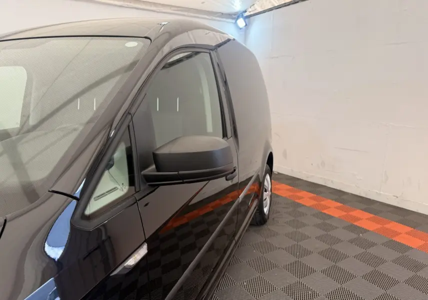 Vue de profil côté gauche d’un Volkswagen Caddy noir 2019 en intérieur avec sol à damier noir et orange.