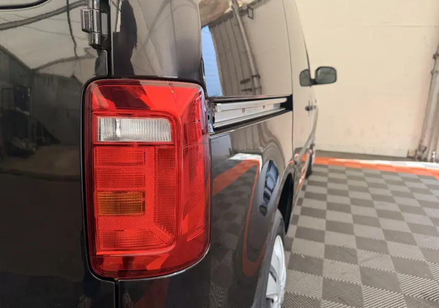 Feu arrière gauche en gros plan du Volkswagen Caddy noir, vue latérale arrière droite dans un garage.