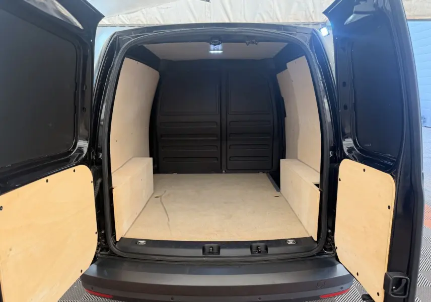 Vue arrière ouverte du Volkswagen Caddy noir 2019 montrant l'espace de chargement avec revêtement bois clair.