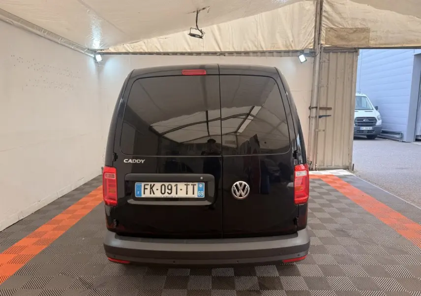 Vue arrière d'un Volkswagen Caddy noir 2019, portes battantes fermées dans un espace couvert avec sol à damier.
