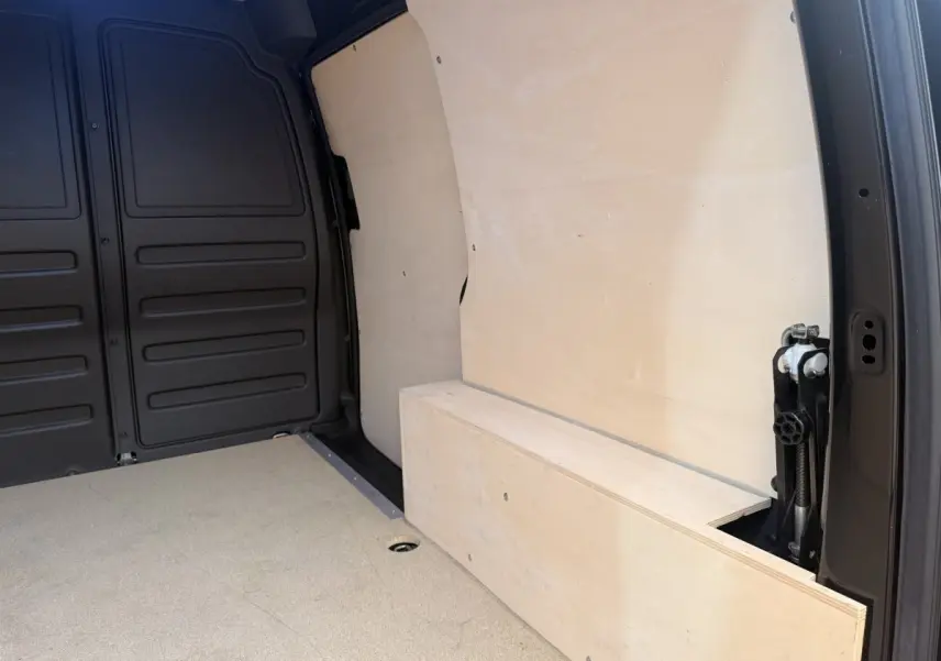 Intérieur du coffre d’un Volkswagen Caddy noir, vue latérale droite montrant la cloison et le plancher en bois clair.