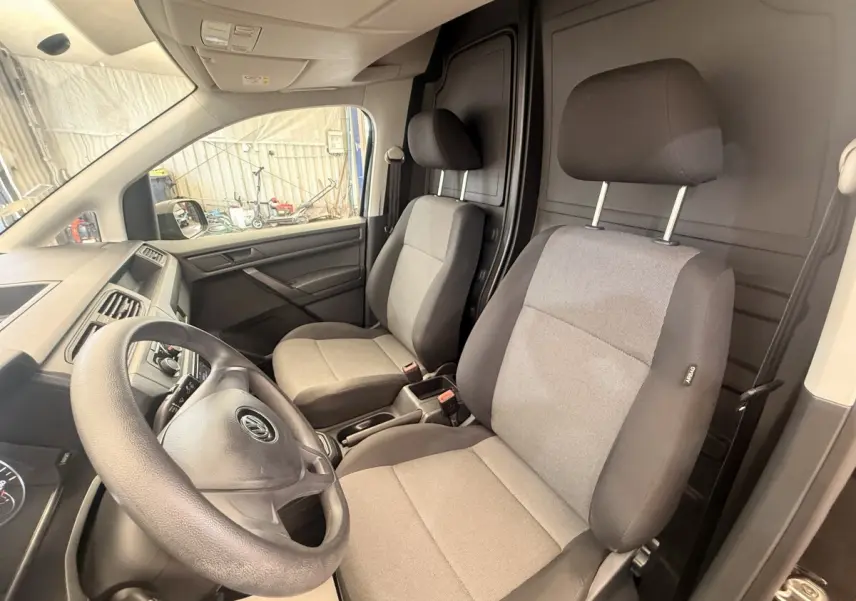 Vue intérieure avant du Volkswagen Caddy 2019 noir, montrant les sièges tissu gris et la cloison pleine noire derrière.