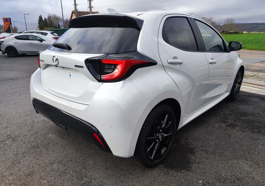 Vue 3/4 arrière droite d'une Mazda2 Hybrid blanc métallisé avec jantes noires et vitres teintées.