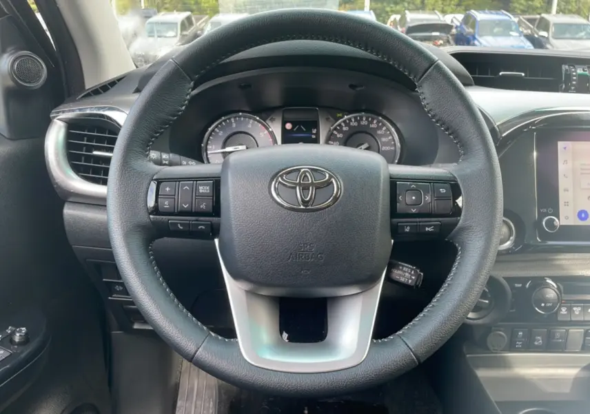 Vue centrée sur le volant noir du Toyota Hilux 2025, avec tableau de bord et commandes visibles en arrière-plan.