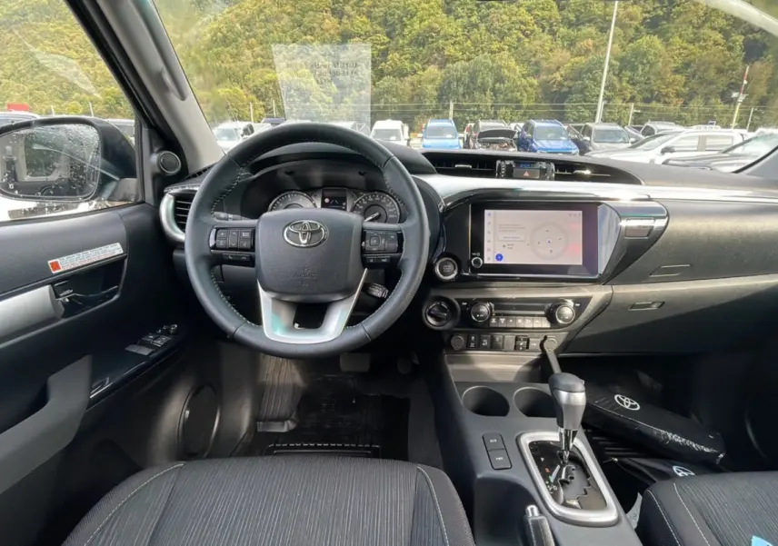 Vue intérieure du tableau de bord et volant du Toyota Hilux 4x4 2025, avec écran tactile et levier de vitesses automatique.