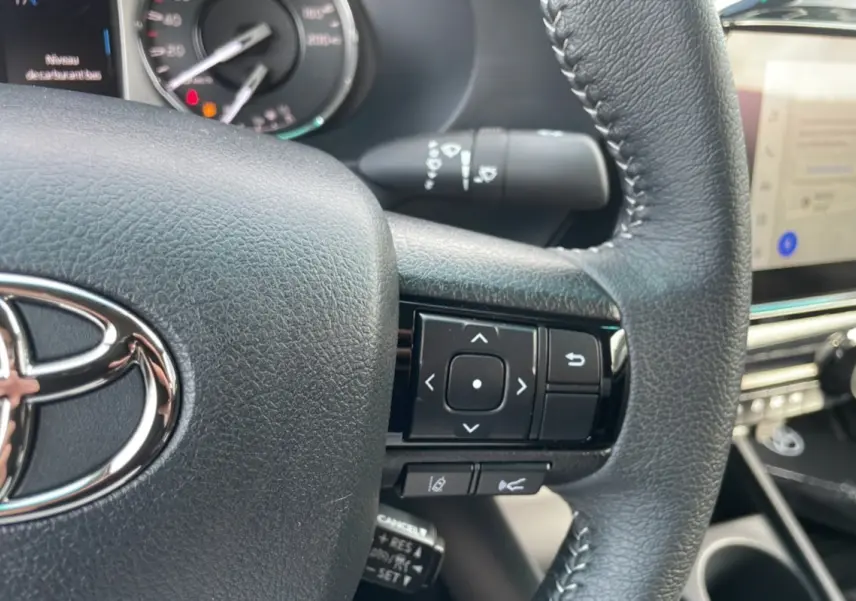Gros plan sur le volant en cuir noir du Toyota Hilux 4x4 2025, avec commandes multifonctions et logo Toyota visible.