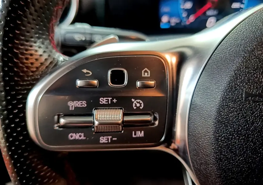 Gros plan sur les commandes du régulateur de vitesse au volant cuir perforé d’une Mercedes Classe A noir 2021.