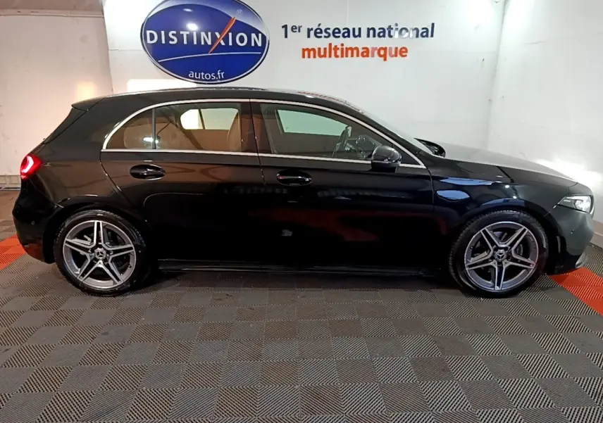 Profil droit d'une Mercedes Classe A 200 AMG Line noire, avec jantes alliage et feux arrière allumés en intérieur showroom.