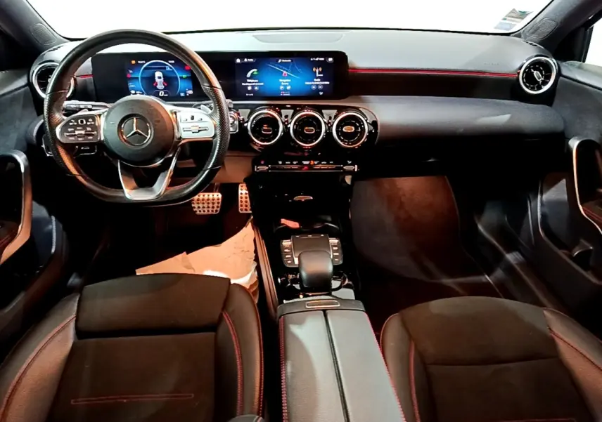 Vue intérieure avant de la Mercedes Classe A A 200 AMG Line 2021, tableau de bord noir avec éclairage rouge et écran tactile large.