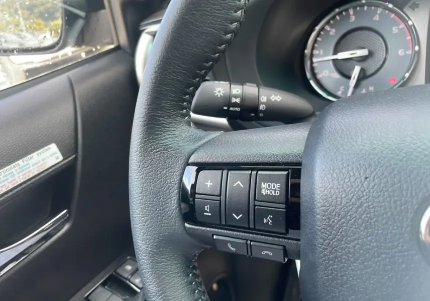 Gros plan sur le volant côté gauche du Toyota Hilux 2025 gris acier, avec commandes audio et tableau de bord en arrière-plan.
