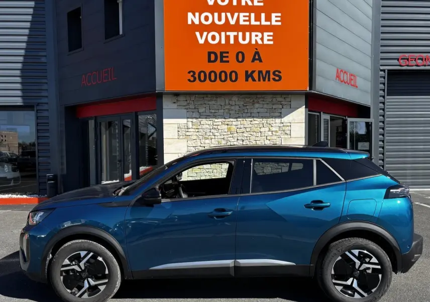Profil latéral gauche d’un Peugeot 2008 bleu métallisé garé devant un bâtiment avec panneau orange.