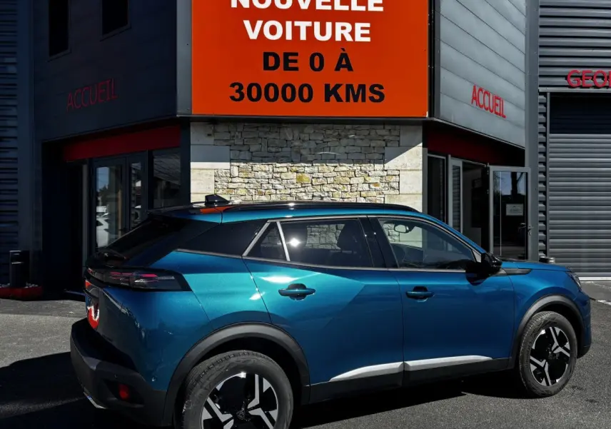 Vue côté droit arrière du Peugeot 2008 Hybrid 145 e-DCS6 Allure bleu métallisé garé devant un bâtiment commercial.