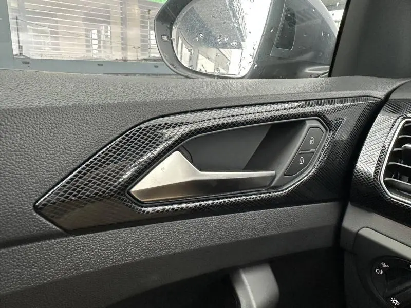 Gros plan sur la poignée intérieure côté gauche du Volkswagen T-Cross 2026 avec insert noir brillant et commandes de verrouillage.