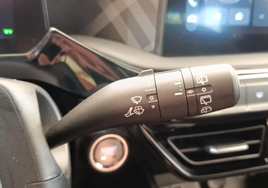 Gros plan sur la commande d’essuie-glace du volant d’une MG3 gris foncé, avec tableau de bord et écran tactile en arrière-plan.