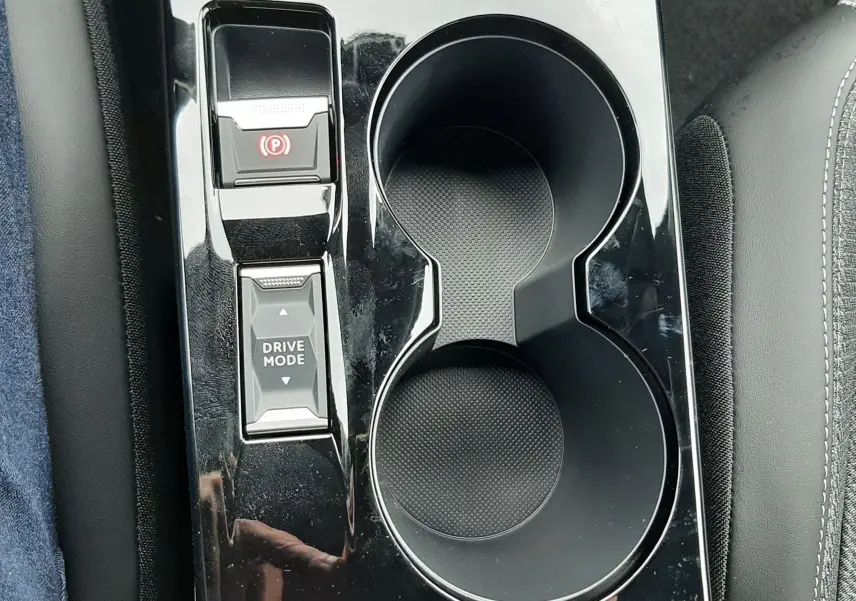 Gros plan sur la console centrale noire brillante du Peugeot 2008 avec porte-gobelets et commandes Drive Mode et frein à main électronique.