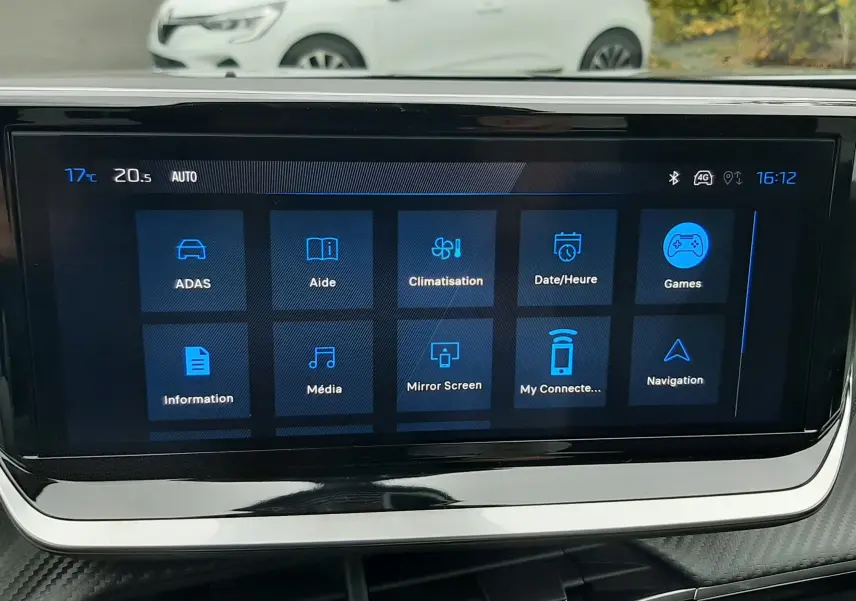 Écran tactile du tableau de bord du Peugeot 2008 gris Artense, avec menu principal et vue extérieure floue en arrière-plan.