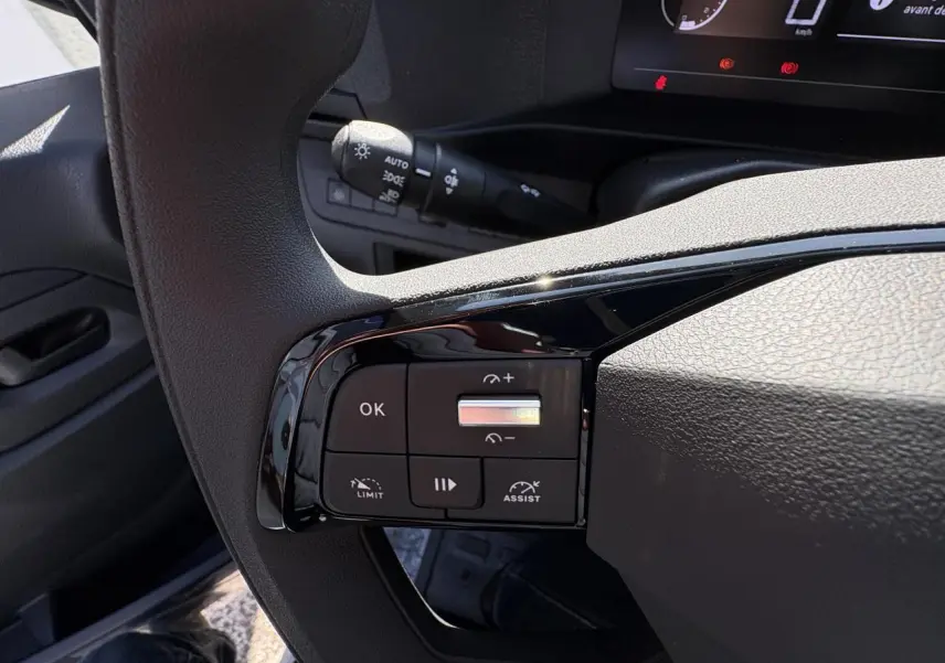 Gros plan sur les commandes au volant à gauche de l’Opel Vivaro blanc, avec tableau de bord numérique en arrière-plan.