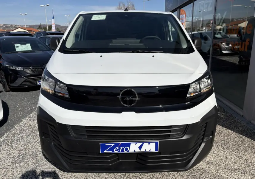 Vue frontale d'un Opel Vivaro blanc 2024 avec calandre noire et plaque "Zéro KM" en concession.