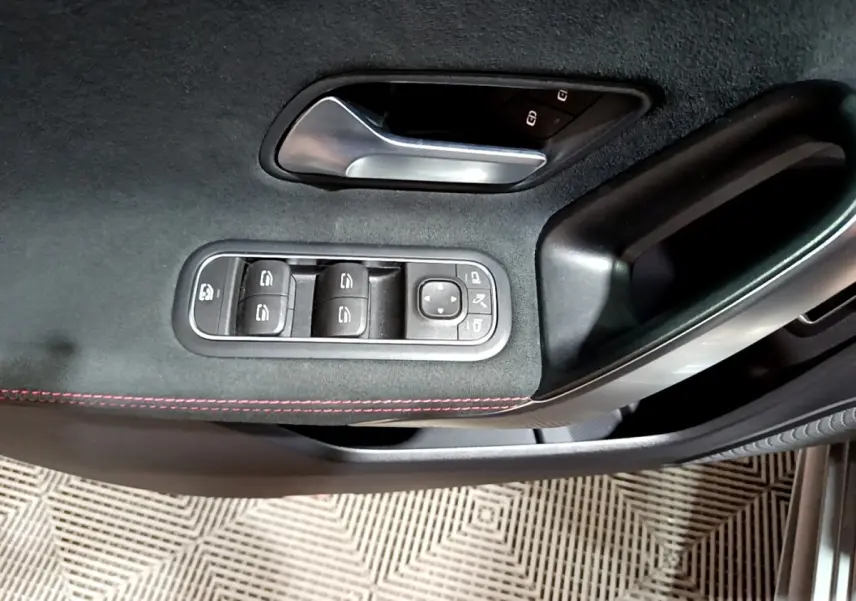 Gros plan sur la commande des vitres et poignée intérieure côté gauche d’une Mercedes Classe A gris foncé AMG Line.