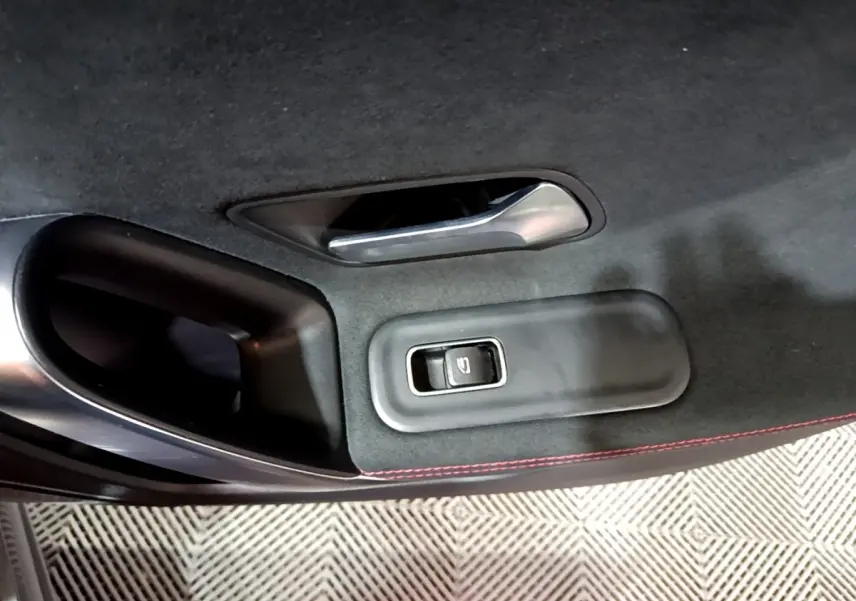 Détail de la porte intérieure côté gauche d’une Mercedes Classe A 250 e AMG Line 2021 gris foncé avec bouton de lève-vitre et surpiqûres rouges.