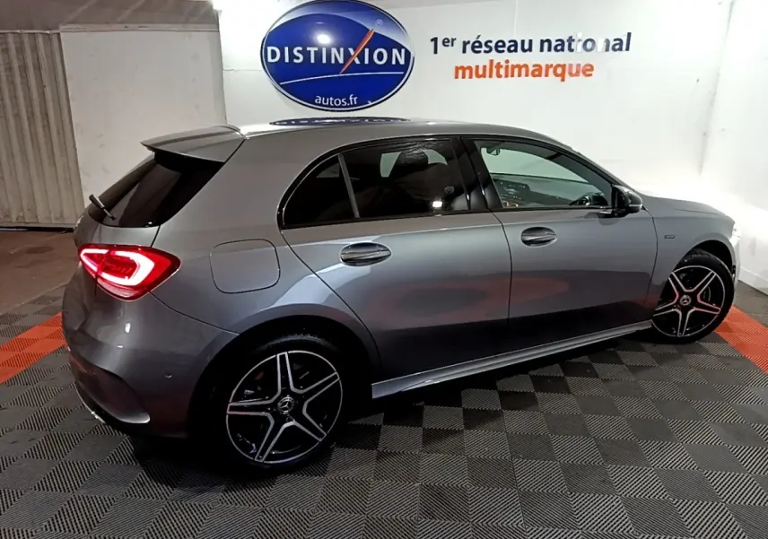 Vue latérale droite d'une Mercedes Classe A 250 e AMG Line gris foncé avec feux arrière LED allumés en intérieur showroom.