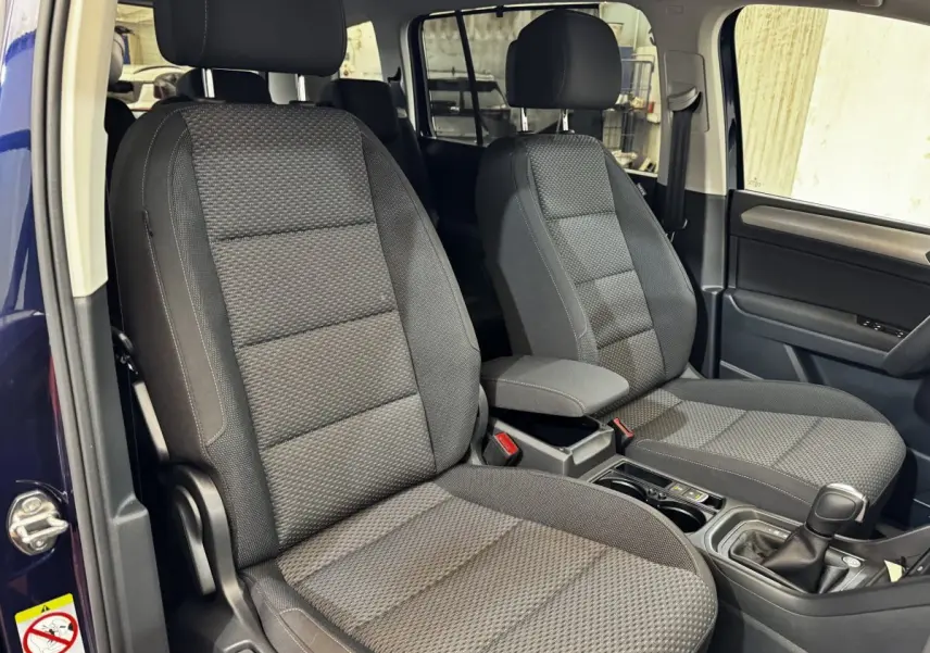 Vue intérieure côté avant droit du Volkswagen Touran bleu 2024, montrant les sièges tissu gris et la console centrale.