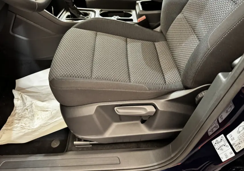 Gros plan sur le siège avant droit tissu gris foncé du Volkswagen Touran 2024, avec réglage manuel et partie de la portière bleue visible.