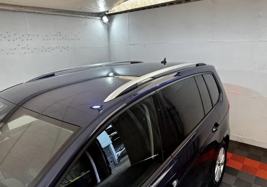 Vue en plongée côté droit du Volkswagen Touran bleu 2024 avec barres de toit argentées et toit panoramique.