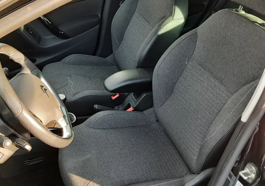 Vue intérieure côté conducteur de la Citroën C3 noire, sièges en tissu gris et volant avec commandes intégrées.