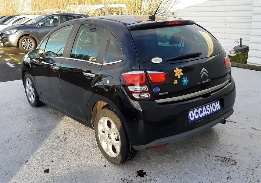 Citroën C3 noire vue 3/4 arrière droit avec autocollants colorés sur le hayon et plaque "OCCASION".