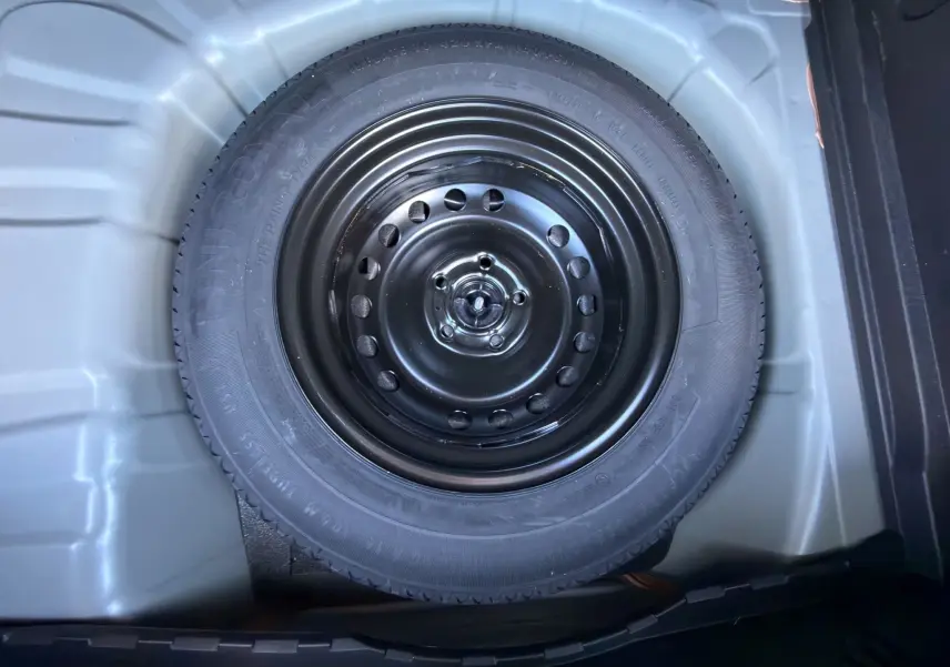 Pneu de secours noir dans le coffre d’un Renault Captur 2024 gris Cassiopée avec toit noir, vue de dessus.