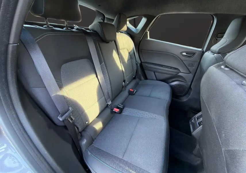 Vue intérieure arrière côté gauche du Renault Captur 2024, sièges tissu gris avec surpiqûres bleues et ceinture de sécurité.
