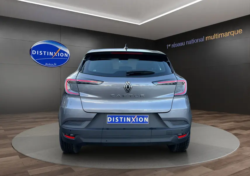 Vue arrière du Renault Captur 2024 gris Cassiopée avec toit noir, feux LED et logo distinctif sur fond showroom.