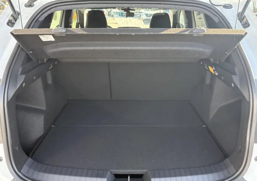 Coffre ouvert vu de l'arrière d'un Dacia Duster blanc métallisé avec cache-bagages relevé et banquette arrière visible.