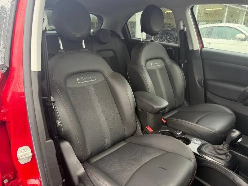 Vue intérieure côté gauche de la FIAT 500X 2024 rouge Passione, sièges noirs avec logo 500 brodé et surpiqûres rouges.