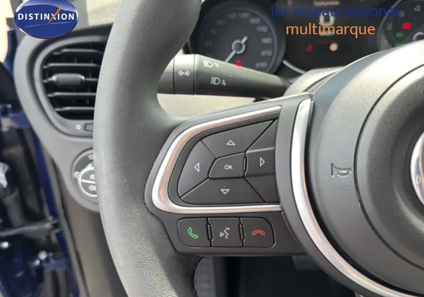 Gros plan sur le volant avec commandes intégrées du Fiat 500X bleu Venezia, tableau de bord partiellement visible en arrière-plan.