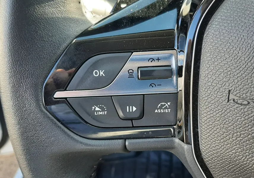 Gros plan sur les commandes de régulateur de vitesse au volant noir d’une Peugeot 308 blanche 2024.