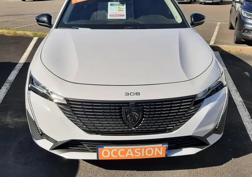 Vue avant d'une Peugeot 308 blanche 2024 avec calandre noire et plaque "OCCASION" en orange, en extérieur.